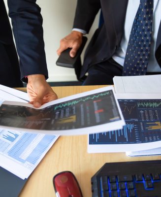 Investor and trader discussing statistic data, holding papers with financial charts and pen. Cropped shot. Broker job or trading concept