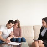 Happy young couple signing documents on meeting with real estate agent, young man putting signature on contract of purchase, buying property, first mortgage investment, prenuptial agreement